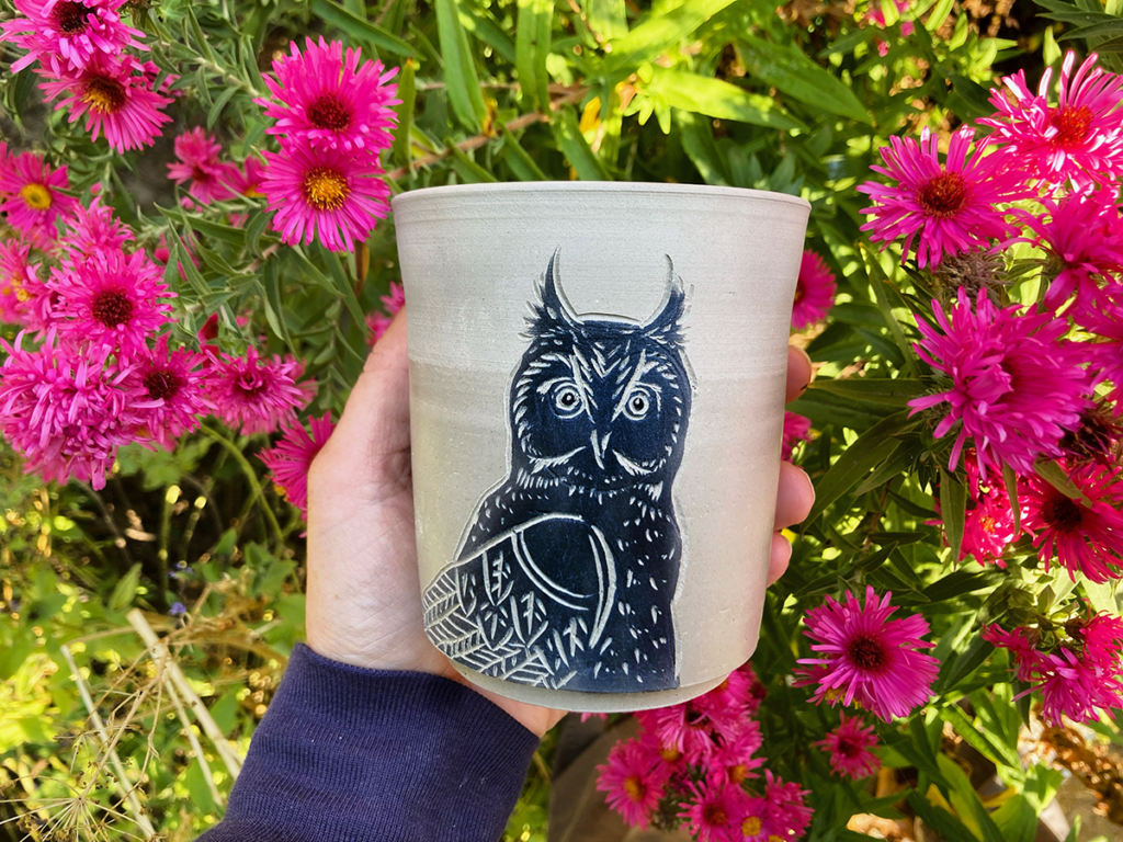 Mug, before firing, painted with an owl. In front of pink flowers